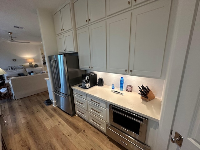 kitchen featuring appliances with stainless steel finishes, tasteful backsplash, ceiling fan, light hardwood / wood-style floors, and white cabinetry