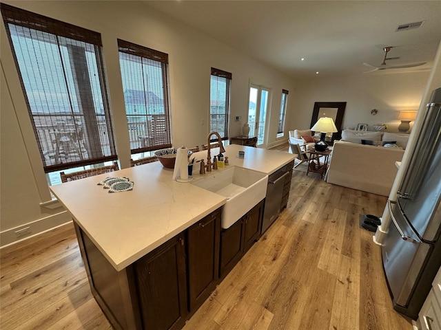 kitchen featuring light wood-type flooring, dark brown cabinetry, ceiling fan, sink, and an island with sink