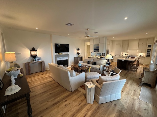 living room with ceiling fan, light wood-type flooring, and a fireplace