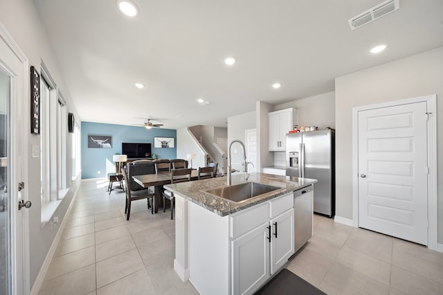 kitchen with dark stone counters, white cabinets, a center island with sink, sink, and ceiling fan