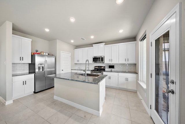 kitchen featuring appliances with stainless steel finishes, sink, a center island with sink, dark stone countertops, and white cabinets