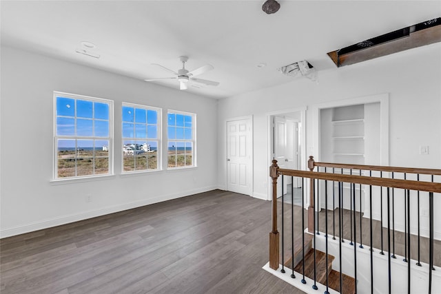 empty room featuring built in shelves, dark hardwood / wood-style flooring, and ceiling fan