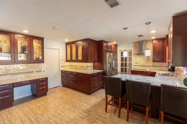 kitchen with a peninsula, visible vents, built in study area, stainless steel fridge with ice dispenser, and wall chimney exhaust hood