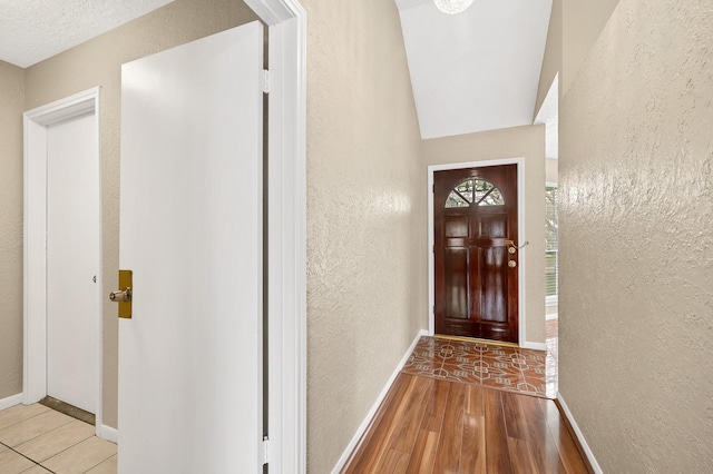 entryway featuring vaulted ceiling, a textured ceiling, and light hardwood / wood-style flooring