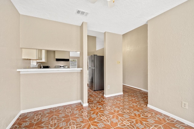 interior space featuring stainless steel refrigerator, ceiling fan, tile patterned flooring, cream cabinets, and a textured ceiling