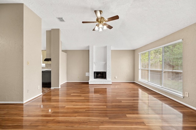 unfurnished living room with hardwood / wood-style flooring, ceiling fan, a textured ceiling, and a brick fireplace