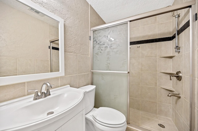 bathroom featuring a textured ceiling, vanity, a shower with door, tile walls, and toilet