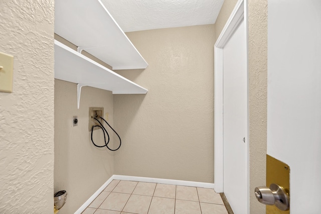 clothes washing area with hookup for an electric dryer, light tile patterned floors, a textured ceiling, and hookup for a washing machine