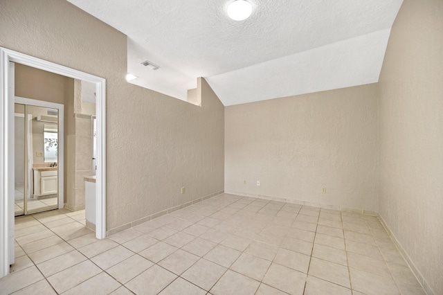 spare room with a textured ceiling, light tile patterned flooring, and lofted ceiling