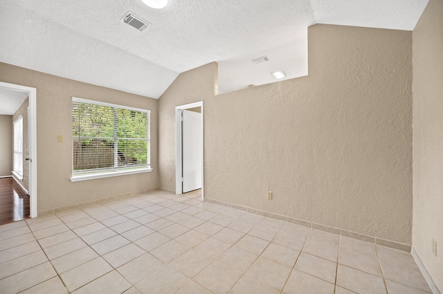 spare room with a textured ceiling, light tile patterned flooring, and vaulted ceiling