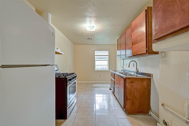 kitchen featuring stainless steel gas range oven, a textured ceiling, light tile patterned floors, white refrigerator, and sink