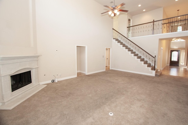 unfurnished living room featuring a towering ceiling, ceiling fan, and carpet flooring