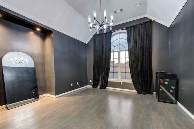 empty room featuring a chandelier, hardwood / wood-style flooring, vaulted ceiling, and ornamental molding