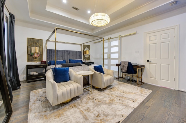 bedroom with hardwood / wood-style floors, a barn door, crown molding, and a tray ceiling