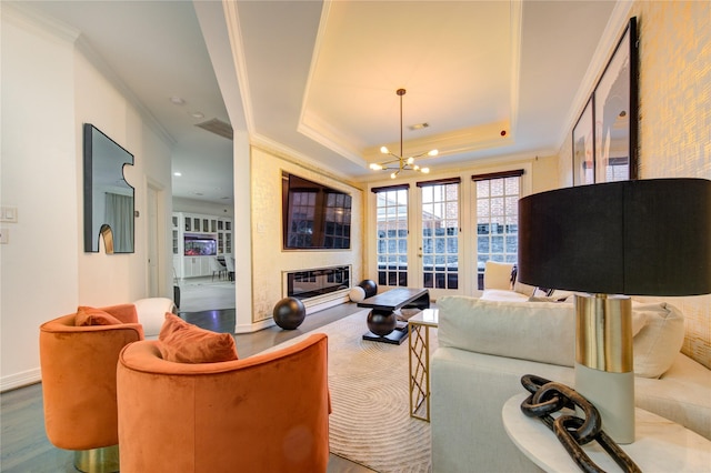 living room with french doors, ornamental molding, a raised ceiling, hardwood / wood-style flooring, and a chandelier