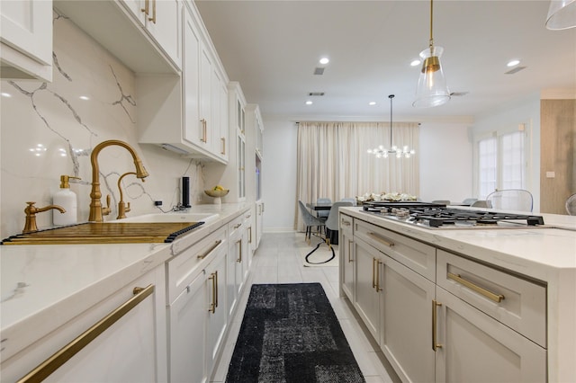 kitchen featuring sink, pendant lighting, stainless steel gas stovetop, decorative backsplash, and white cabinets