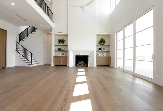 unfurnished living room with ceiling fan, a premium fireplace, light hardwood / wood-style flooring, and a towering ceiling