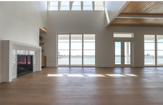 unfurnished living room featuring wooden ceiling, a water view, french doors, hardwood / wood-style flooring, and a high end fireplace