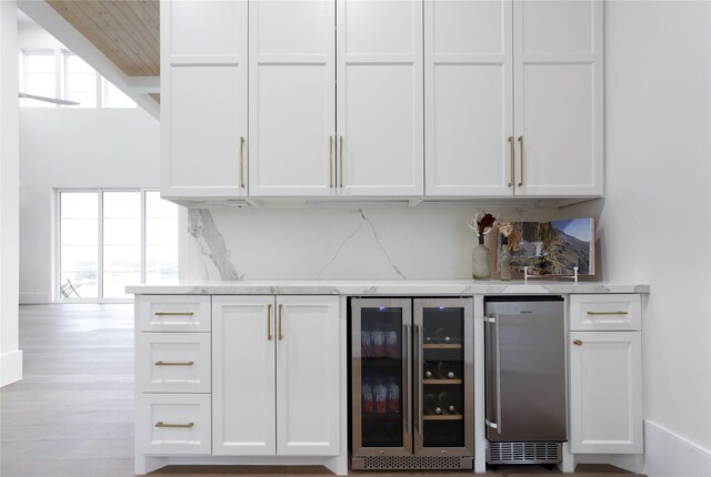 bar featuring white cabinets, plenty of natural light, light stone countertops, and wine cooler