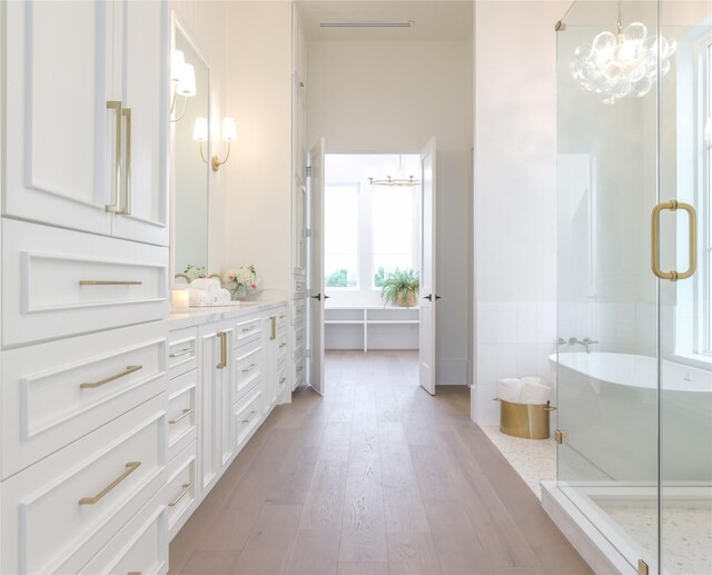 bathroom featuring a chandelier, wood-type flooring, plus walk in shower, vanity, and tile walls