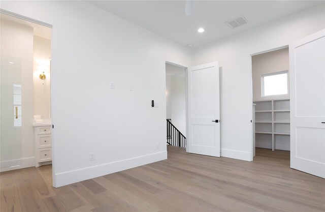 unfurnished bedroom featuring a walk in closet, light wood-type flooring, a closet, and connected bathroom