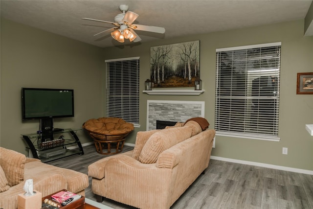 living room with light wood-type flooring, ceiling fan, a textured ceiling, and a stone fireplace