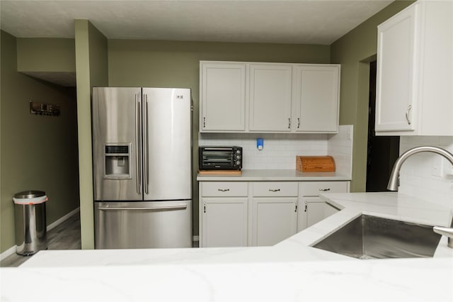 kitchen with sink, tasteful backsplash, white cabinets, and stainless steel refrigerator with ice dispenser