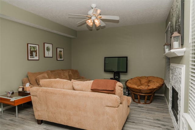 living room with a fireplace, ceiling fan, a textured ceiling, and light hardwood / wood-style flooring