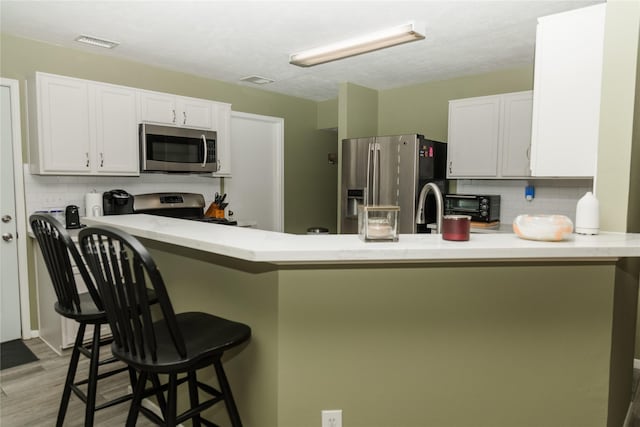 kitchen with white cabinets, kitchen peninsula, decorative backsplash, a breakfast bar, and appliances with stainless steel finishes