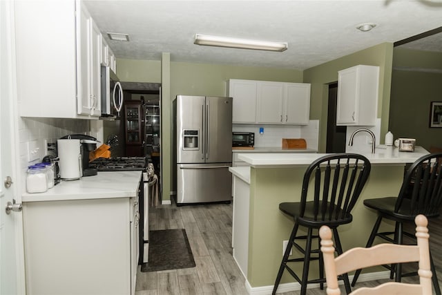 kitchen featuring kitchen peninsula, stainless steel appliances, white cabinets, and a kitchen breakfast bar