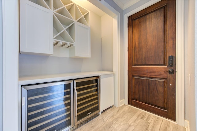 bar with white cabinetry, beverage cooler, and light wood-type flooring