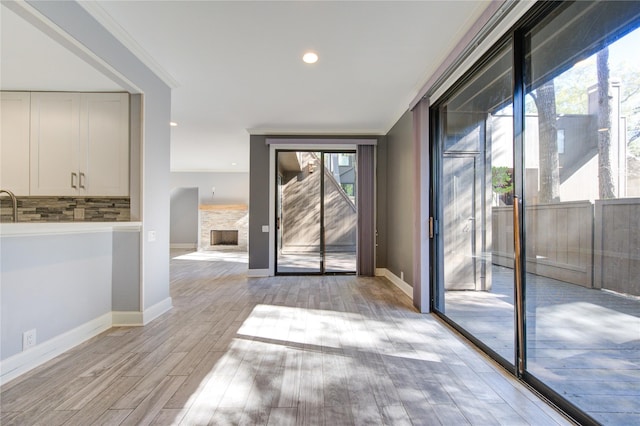 doorway with a fireplace, light hardwood / wood-style floors, crown molding, and a wealth of natural light