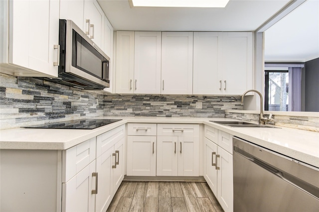 kitchen featuring light wood-type flooring, backsplash, stainless steel appliances, sink, and white cabinets