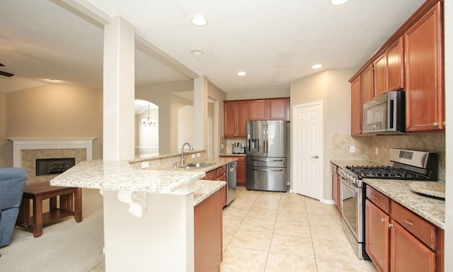 kitchen with a tile fireplace, sink, light stone counters, decorative backsplash, and appliances with stainless steel finishes