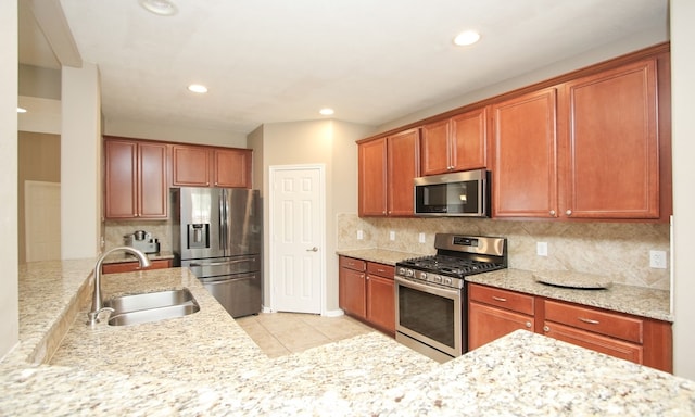 kitchen with sink, light stone countertops, light tile patterned floors, tasteful backsplash, and stainless steel appliances