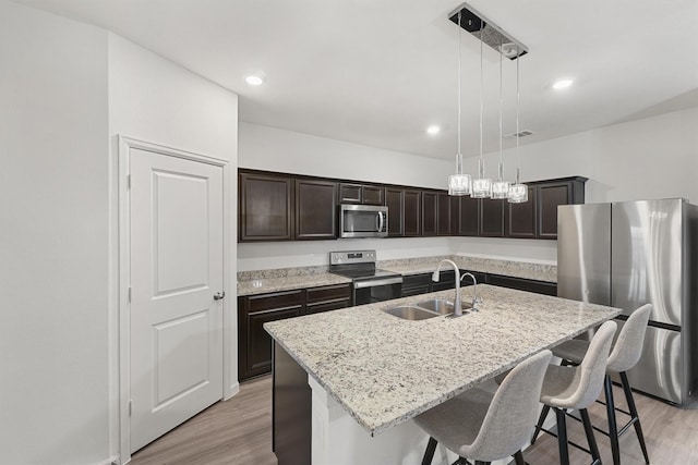 kitchen featuring pendant lighting, an island with sink, light hardwood / wood-style floors, appliances with stainless steel finishes, and sink