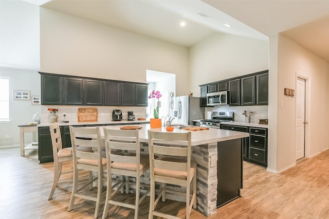 kitchen featuring high vaulted ceiling, light wood-type flooring, an island with sink, a kitchen bar, and stainless steel appliances