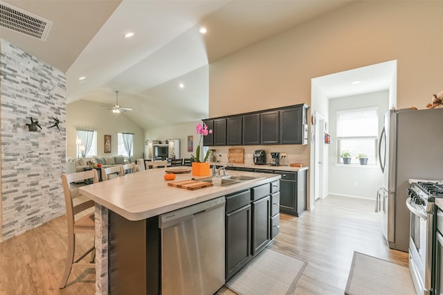 kitchen with ceiling fan, a kitchen breakfast bar, an island with sink, lofted ceiling, and appliances with stainless steel finishes