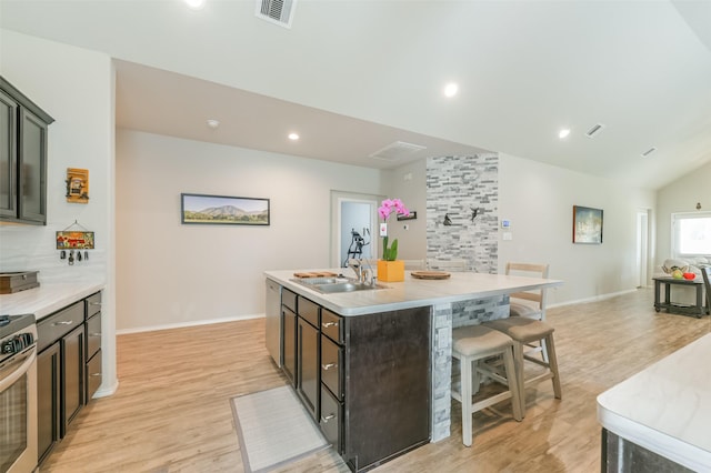 kitchen with lofted ceiling, a center island with sink, a kitchen breakfast bar, sink, and light hardwood / wood-style flooring