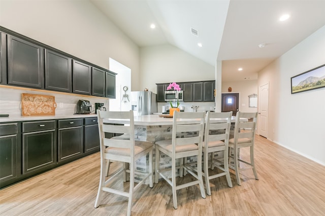 kitchen featuring a center island, light wood-type flooring, stainless steel appliances, and high vaulted ceiling