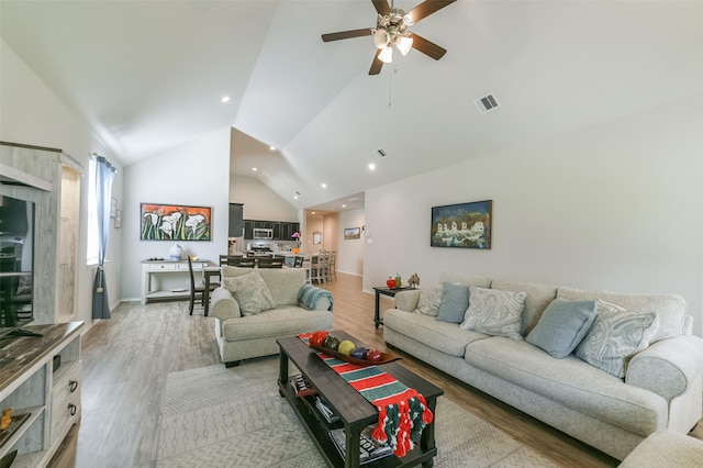 living room with ceiling fan, high vaulted ceiling, and light hardwood / wood-style flooring