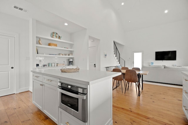 kitchen with white cabinetry, stainless steel oven, a center island, decorative backsplash, and light wood-type flooring