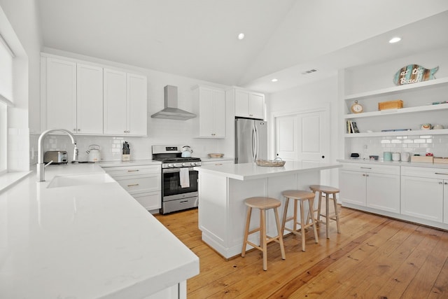 kitchen with appliances with stainless steel finishes, a kitchen island, white cabinetry, and wall chimney exhaust hood