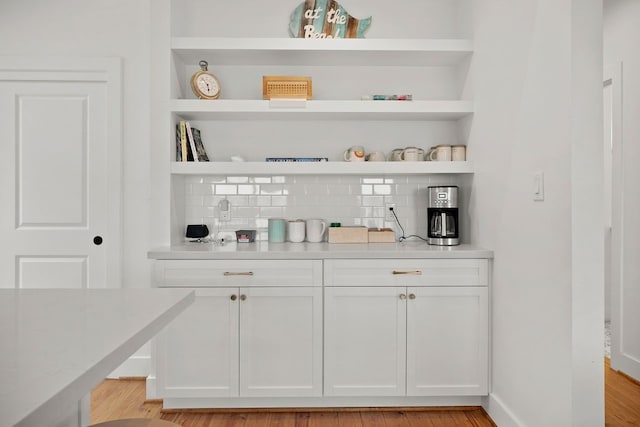 bar with tasteful backsplash, white cabinets, and light hardwood / wood-style floors