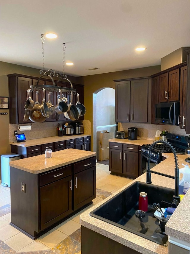 kitchen featuring arched walkways, range with gas cooktop, stainless steel microwave, a center island, and dark brown cabinets