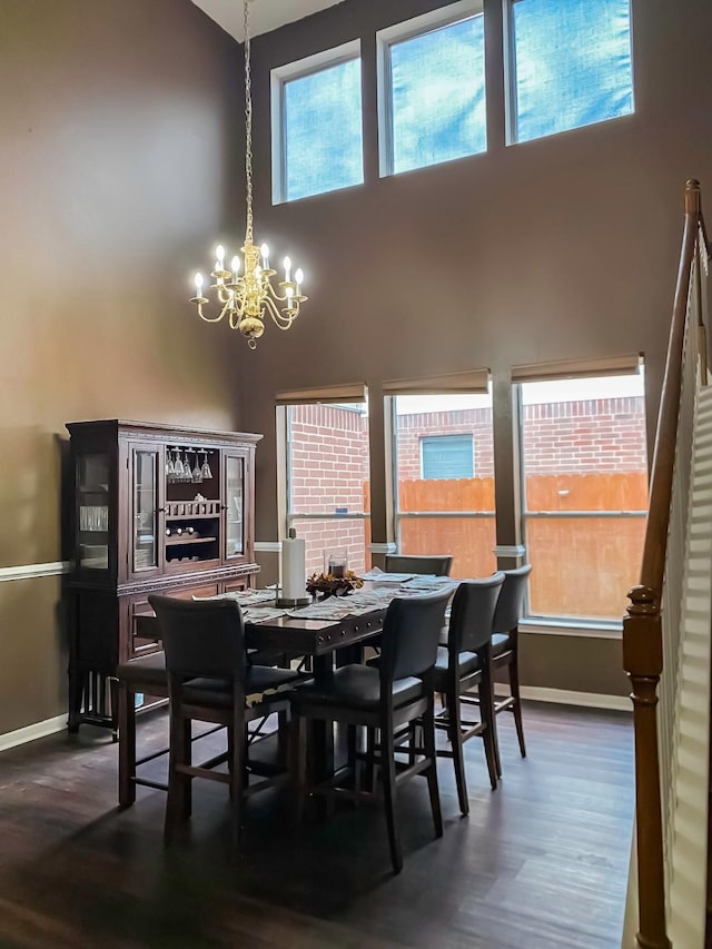 dining room with a towering ceiling, an inviting chandelier, baseboards, and wood finished floors