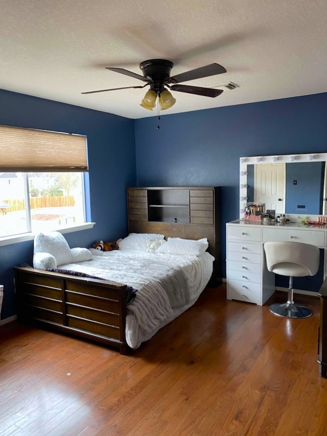 bedroom with a ceiling fan, a textured ceiling, visible vents, and hardwood / wood-style floors