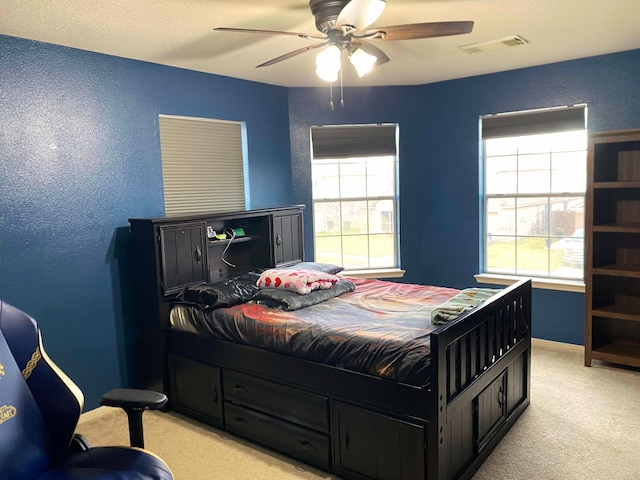 bedroom featuring ceiling fan, multiple windows, visible vents, and light colored carpet