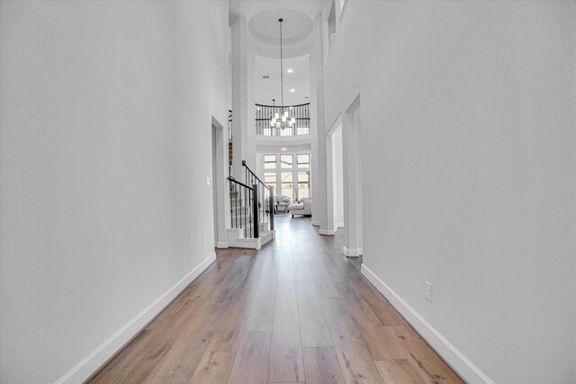 hall with a towering ceiling, an inviting chandelier, and light wood-type flooring