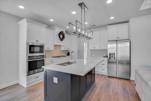 kitchen with light hardwood / wood-style flooring, pendant lighting, stainless steel appliances, an island with sink, and white cabinets